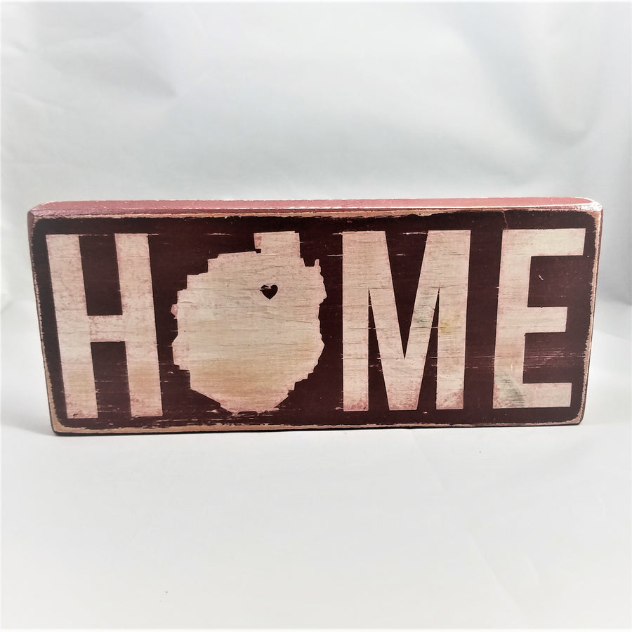 Red wood sign standing upright with white letter. The O in HOME is the shape of the Adirondack Park with a heart in the upper right side
