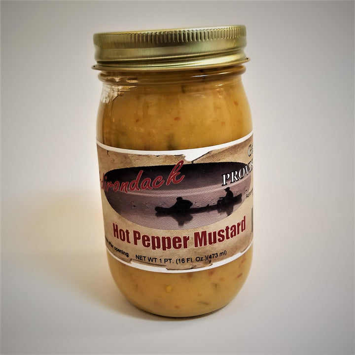 Clear jar of Hot Pepper Mustard with Adirondack Provisions label in the front center. Yellow mustard with red pepper specks show through the clear jar above the label. Gold screw top.