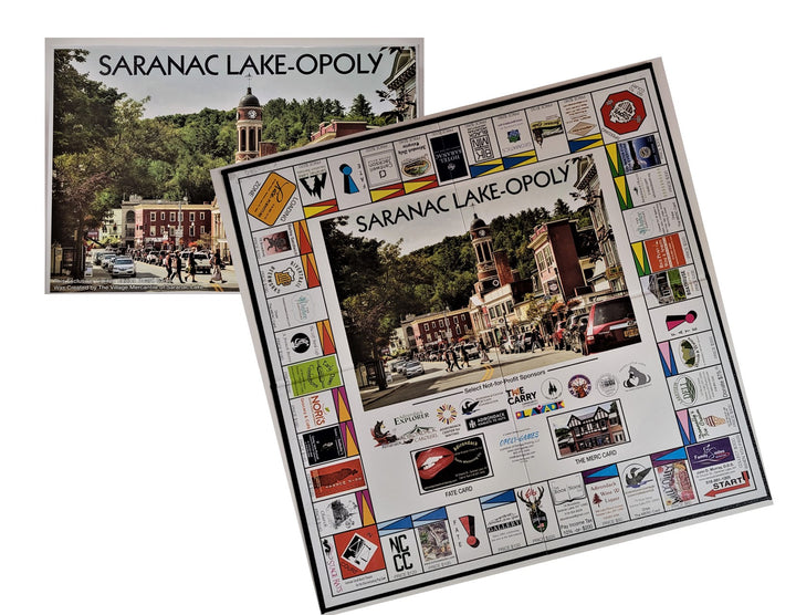 Saranac Lake-Opoly box with bottom right side covered by the open game board. SARANAC LAKE-OPOLY printed in center over a photo of the center of town with all of the participating businesses in town on various property rectangles on the gameboard.