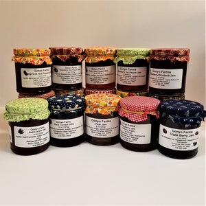 10 Gonyo Farms jams  stacked and facing front. Each has a colorful cloth fixed over the top and a while label describing what's inside.