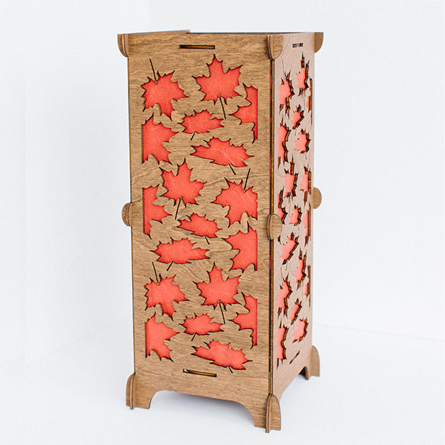 Standing art lamp with orange cut out leaves in a wooden rectangular base.