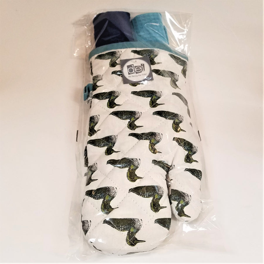 White oven mitt with black and white loons printed all over seen through plastic wrapping.  A light blue hanging loop is on the top left and two blue (one navy, one light) dishtowels are in the mitt opening on the top.