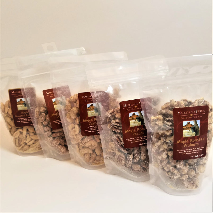Five bags of various Maple Roasted Nuts stand fanned in their clear plastic bags. Labels are centered with nuts showing through the bags.