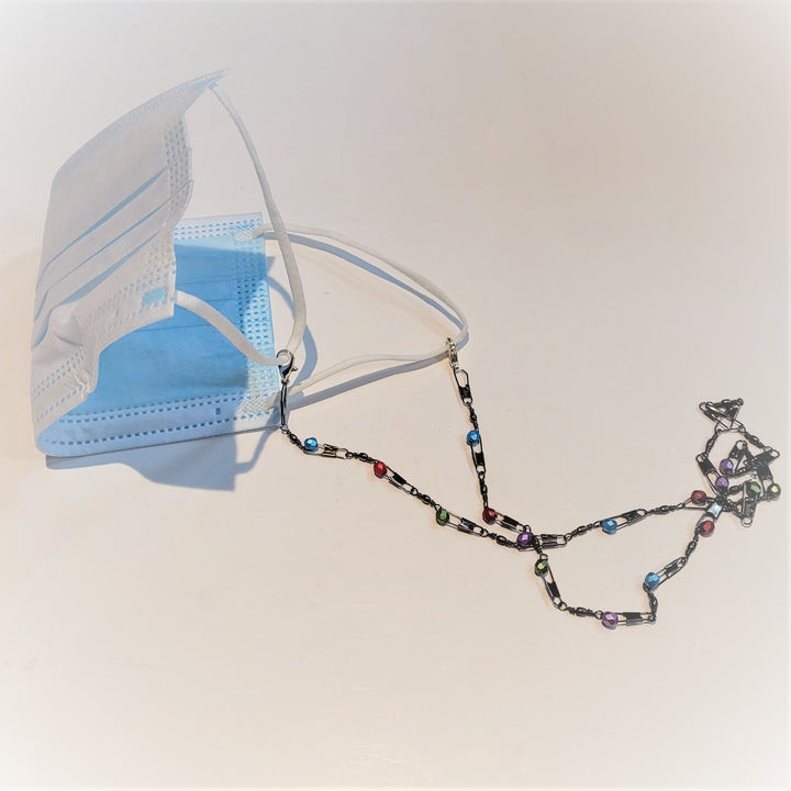 Generic white surgical mask with fishing lures arranged as a mask holder spread out to the right of the mast. Colored glass accents in blue, red, green and purple. 