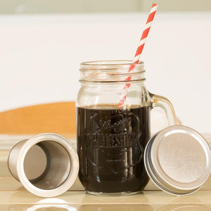 Mason jar 3/4 full of coffee with a red-and-white straw sticking out. The lid of the coffee kit is leaning on the right and the coffee infuser is set to the left of the glass.