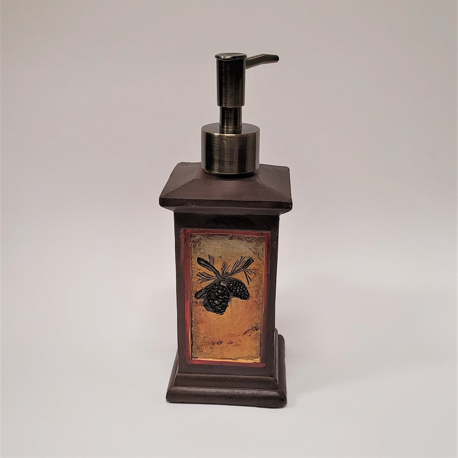 The back of the moose soap dispenser featuring a vertical panel with two pine cones on an amber backing. The metallic push spout is seen from the back.