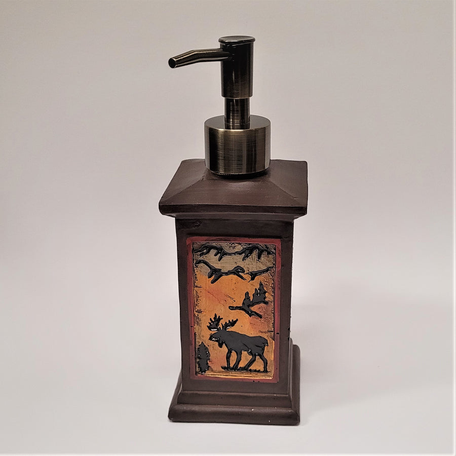 The front of the moose soap dispenser. A dark rectangular standing dispenser with a vertical, rectangular picture of a moose in amber shades under the metallic push spout.