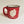 A single red-with-black speckled camp mug with the words SARANAC LAKE, NY on the bottom and a white-filled outline of the Adirondack Park in the center. There is a small red heart in the white outline located where Saranac Lake sits. The mug has a black rim and white interior.