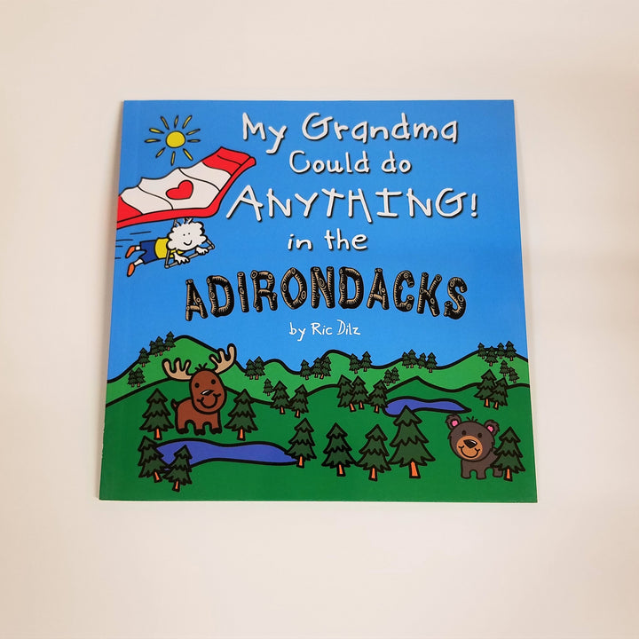 Cover of the square book, My Grandma Could Do Anything in the Adirondacks with type displayed in white lettering and wood-style font for Adirondacks. The cover drawing includes a bright blue sky with small yellow sun and a person attached to a hang glider soaring over green mountains, evergreens , a moose and a bear.