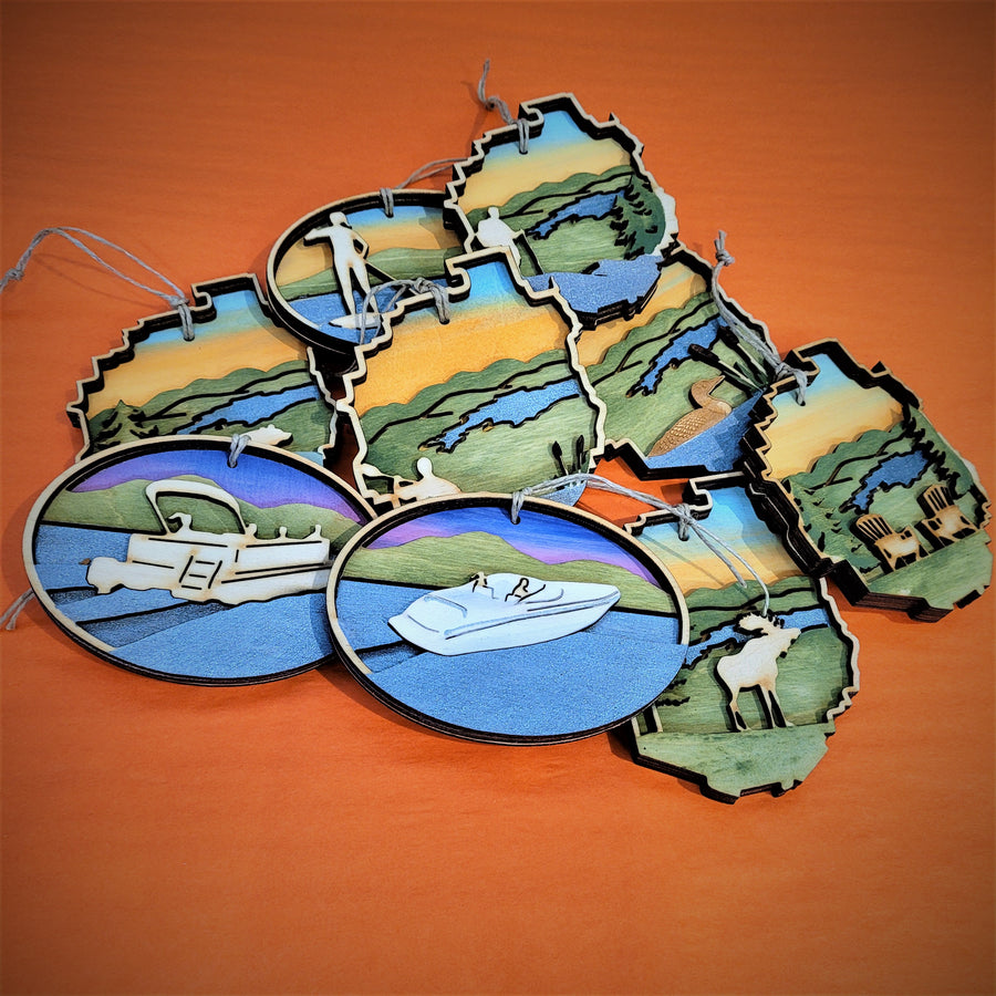 Oval and Adirondack Park shaped ornaments spread on an orange background. In the foreground from left to right is a pontoon boat ornament, a motor boat, a moose and a pair of Adirondack chairs.  Above those from right to left a loon and a paddler ornament. Above that from left to right only the blue water and golden sky can be seen furthest to the left then a standing paddler and a hiker.