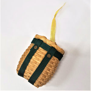 Tiny pack basket with green straps pictured flat and tilted with gold ribbon stretched out above the basket.