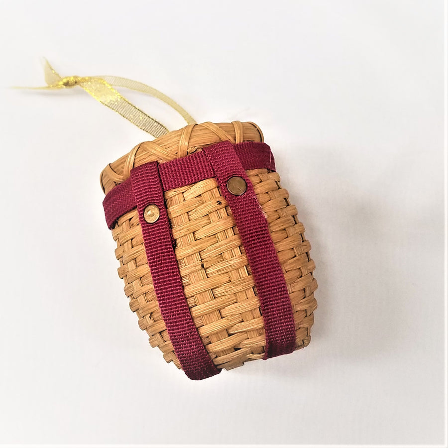 Tiny pack basket with red straps pictured flat and tilted with gold ribbon stretched out above the basket.
