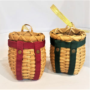 Two tiny pack baskets. One on left with red straps and on the right green straps. Each basket has two gold circles embedded on the straps just below where they meet. Each has a gold ribbon for hanging seen on the top of the basket.