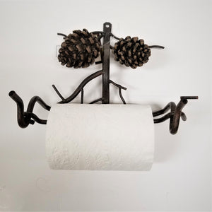 Metal toilet paper holder with two pine cones on top pictured with toilet paper