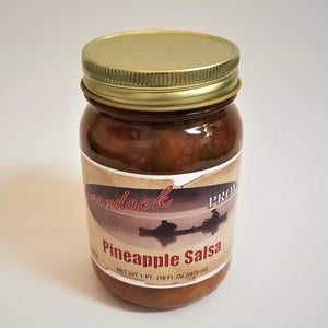 Glass jar of Pineapple Salsa. Red sauce with glimpses of seeds and yellow can be seen through the glass under the gold screw top.