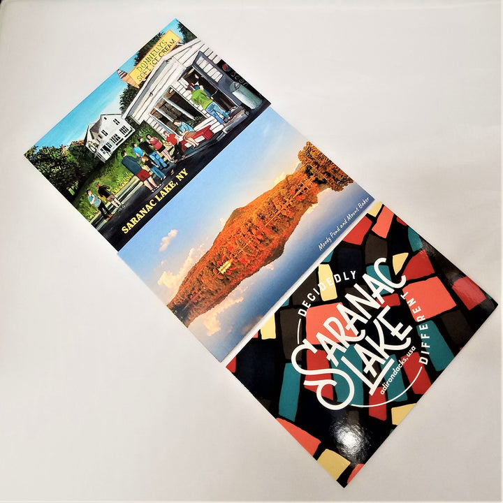 Three postcards laid out on a diagonal--top features Donnelly's Ice Cream Stand by Matt Burnett, middle features a reflective photograph of Moody Pond and Mount Baker; bottom features the Saranac Lake Decidedly Different Puzzle Logo