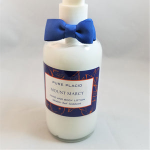Clear bottle of Pure Placid Mount Marcy Hand and Body Lotion standing. The white cream shows through around the label of the bottle which is topped with a blue bow tie.
