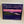 Box cover of Adirondack Panoramic Jigsaw Puzzle: Sunset Over Fourth Lake features a horizontal photo with purple sky over dark mountains and lake with a foreground of dark greenery surrounding the water.
