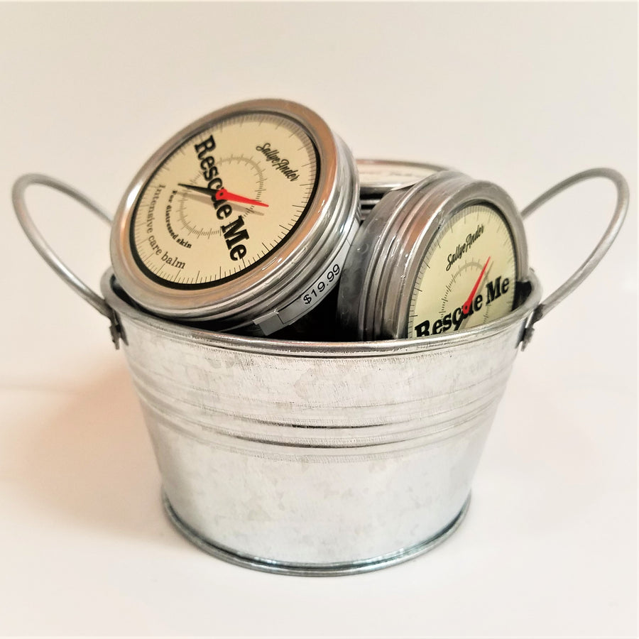 Silver bucket filled with silver circular containers of Rescue Me. The top of the container looks like a compass face with black text on an off-white background.