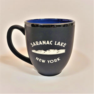 Black bistro mug with dark black rim, blue interior peeking through. White lettering SARANAC LAKE above white mountainscape over white lettering NEW YORK.