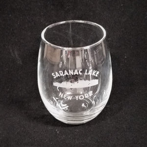 Clear, stemless wine glass with SARANAC LAKE NEW YORK etched in white around white mountains.