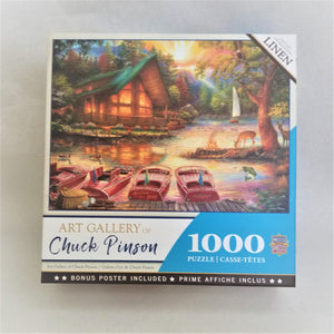 Box cover of 1000 piece jigsaw puzzle featuring an illustration of a camp in the evening with deer grazing near a campfire, red boats at a dock, a sailboat in the water in the distance.