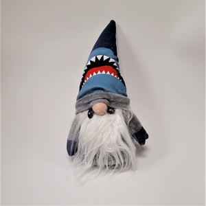 Pointy gnome hat features a set of white teeth below a red mouth or tongue, then black sharp triangles above that on a white panel, then light blue below the dark blue peak. A gray fuzzy band is at the cap bottom resting on the nose. This gnome has a white beard and gray fuzzy arms.