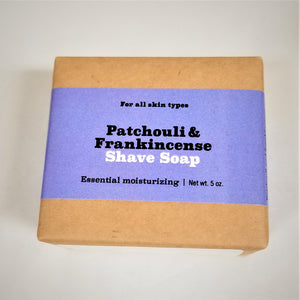 Patchouli and frankincense shave soap flat in its natural wrapping with purple-colored label in center.