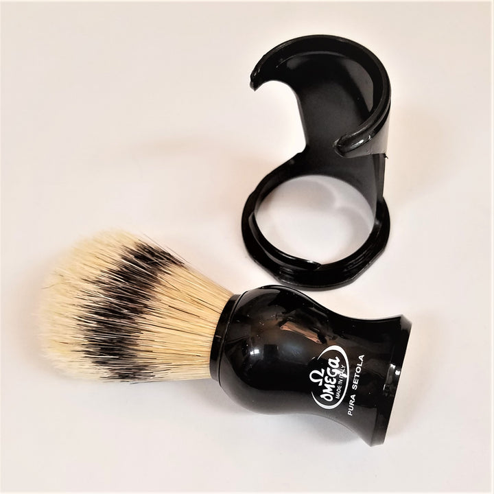 Shaving brush lying flat with black handle to the right and natural and black bristles facing left. Black stand upright in back.