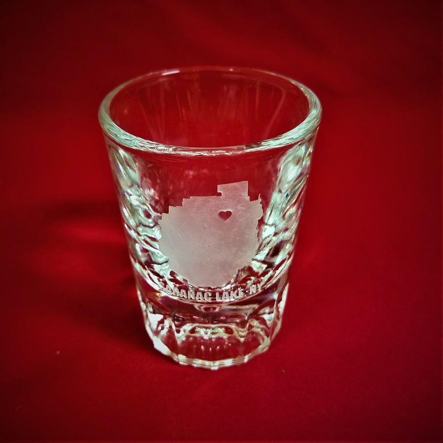 Shot glass on the red back ground with the Adirondack Park etching and red heart of Saranac Lake clearly visible.