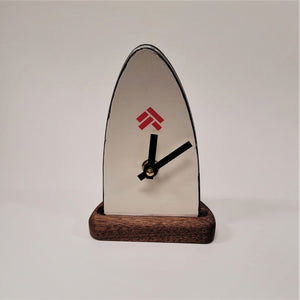 Ski tip clock standing upright, front face. Wood base with white ski tip with black clock hands and a red logo above the black hands.