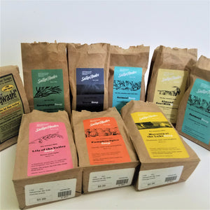 9 bags with labels featuring 9 varieties of SallyeAnder soaps. Beige bags with colorful labels. Six bags standing upright in back; three lying flat in front.