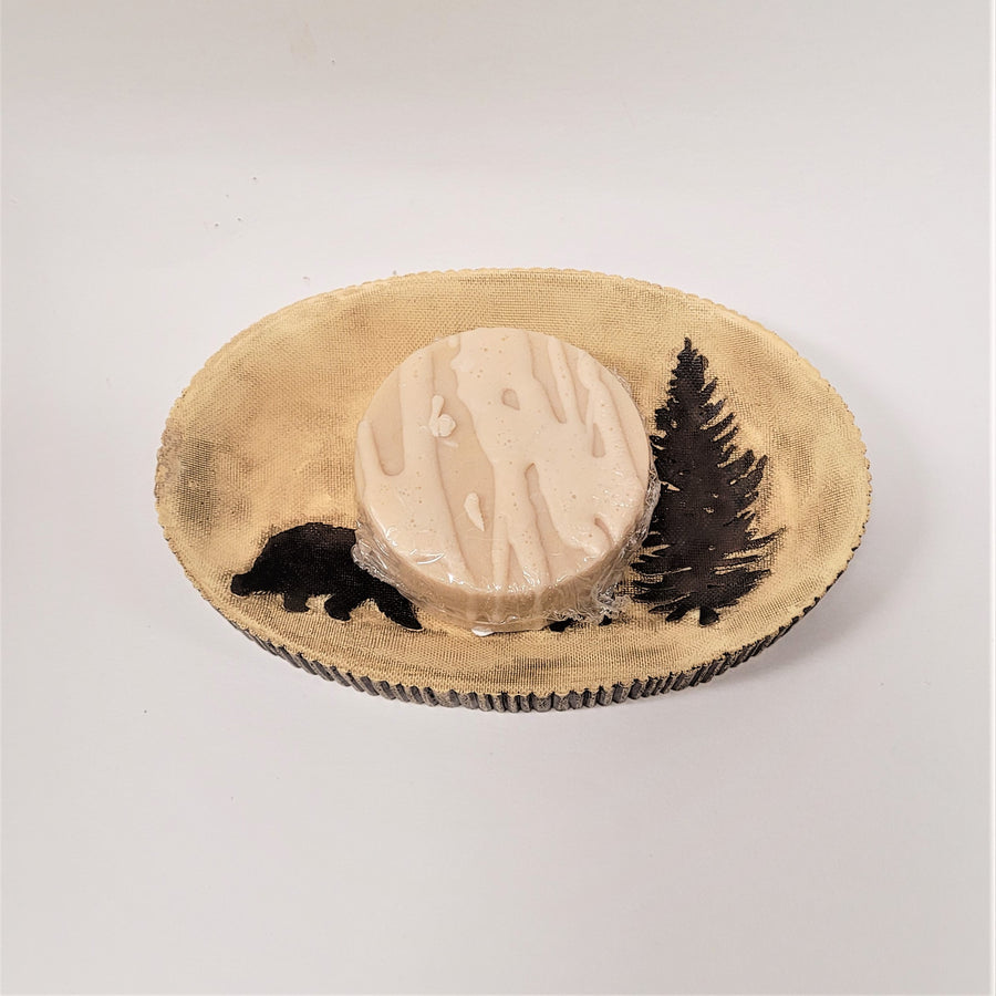 Beige soap dish with some of the oval log-like edging showing on the bottom. Only part of the break and evergreen images are showing under a round of beige-colored soap.