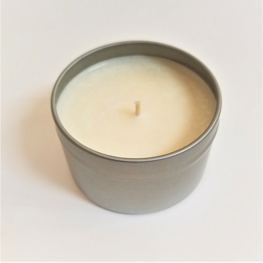 One off-white colored soy candle open in tin base standing upright with wick pointing up
