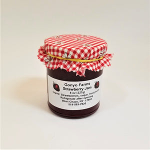 Red checkered cloth with daisy-like flower banded to a jar of Gonyo Farms Strawberry Jam.