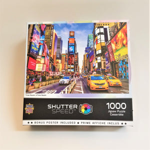 Cover of 1000 piece jigsaw puzzle box featuring a colorful look at NYC's Time Square with taxis and police cars in the street and people on the side walk next to the row of planters.