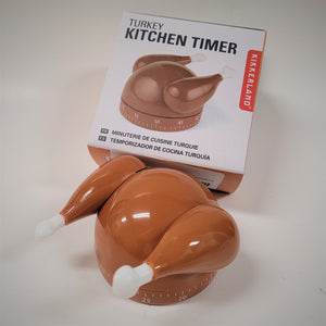 Turkey Kitchen Timer box and brown turkey timer outside the box in front of it. White plastic feet extend from the brown drumsticks. The bottom is the timer, round with numbers and lines for digits in between increments of five.