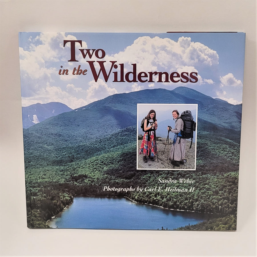 Full-color photograph of mountains and water with an insert of the two women with their hiking gear on the book cover of Two in the Wilderness. 
