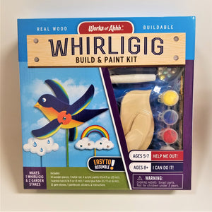 Whirligig Build & Paint Kit in its packaging box. Color print of whirligig in action and pieces of the kit seen through the clear plastic cover: part of the wooden bird, yellow, blue, red paint and a white handle