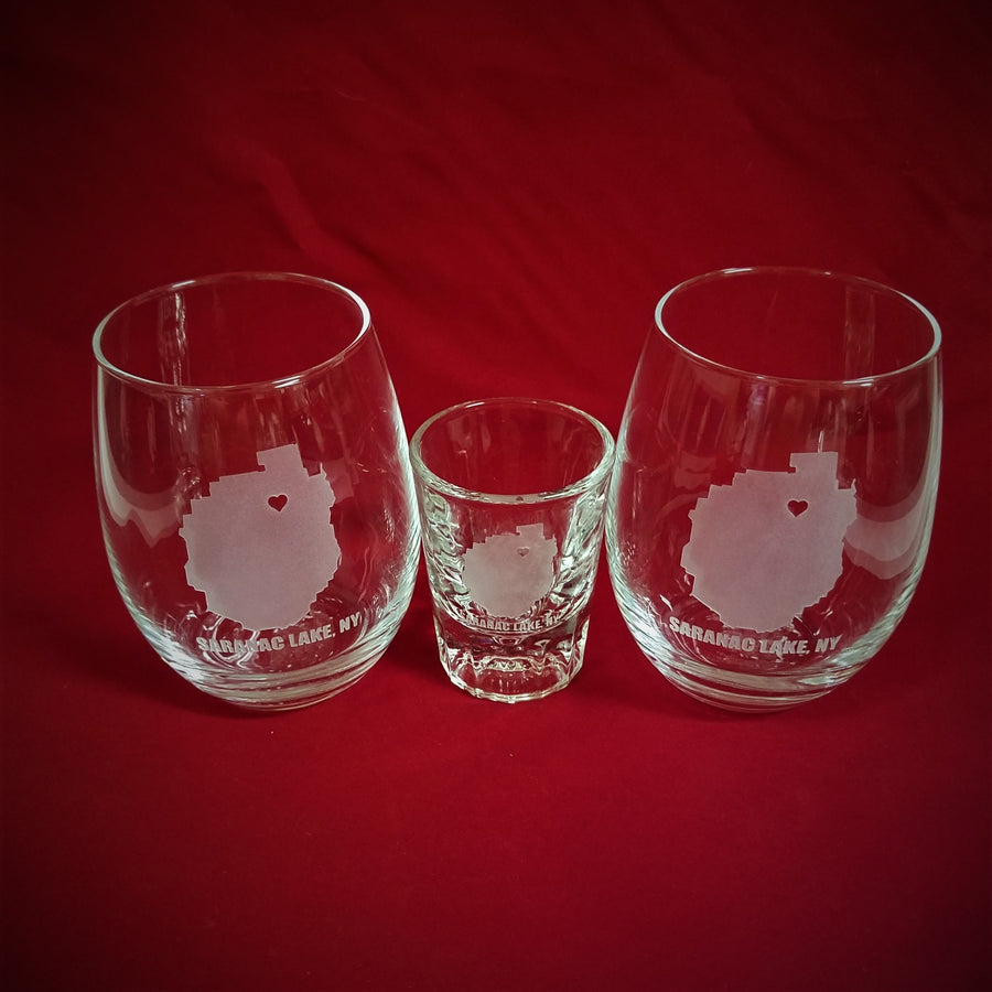Wine Glasses and shot glass with the outline of the Adirondack Park and a heart where Saranac Lake is and the words Saranac Lake, NY etched below. All on a red background to make the etching stand out.