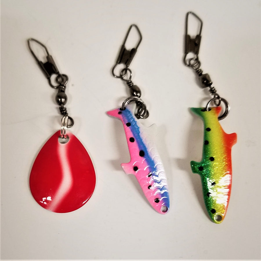 Three fishing lure zipper pulls. Far left, red tear-shaped with white streak in the middle; middle fish-shaped with pink and blue stripes and black speckles; far-right fish-shaped lure with green, yellow, and orange strip with black speckles
