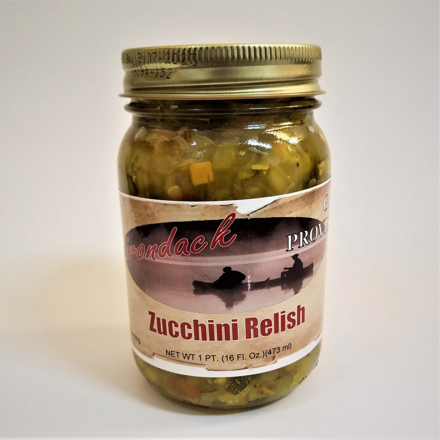 Glass jar of Zucchini Relish. Green and yellow bits with glimpses of seed and orange bits can be seen through the glass under the gold screw top.